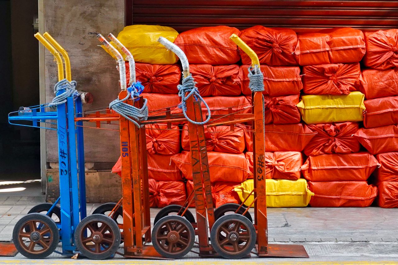 Vibrant hand trucks lined up against stacked colorful sacks in an industrial setting.