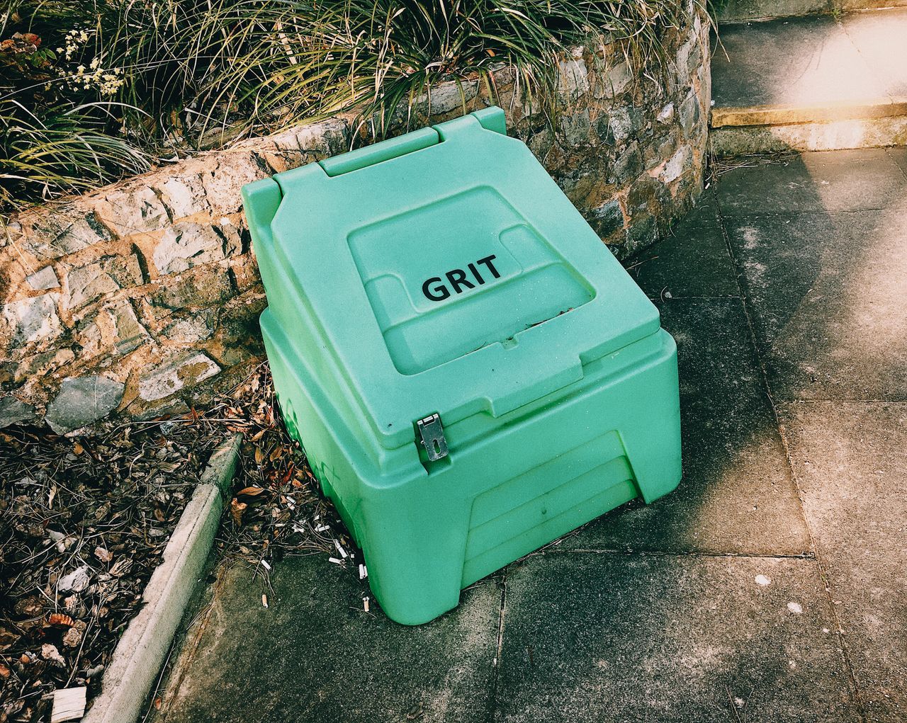 High angle of plastic container with grit on paved surface near entrance of building